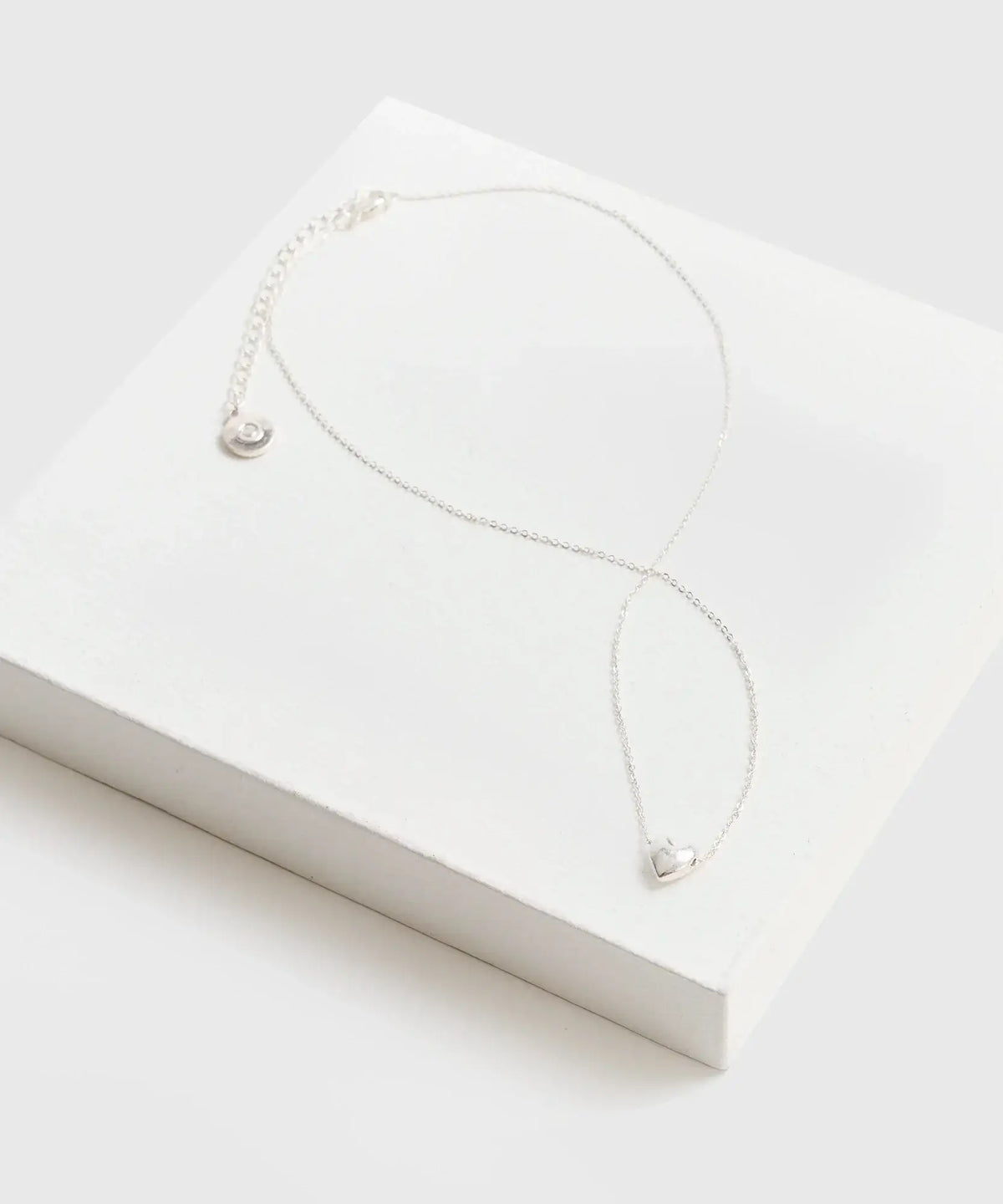Collar Corazón de cadena delgada con charm de corazón de la marca Lounge sobre una caja blanca.