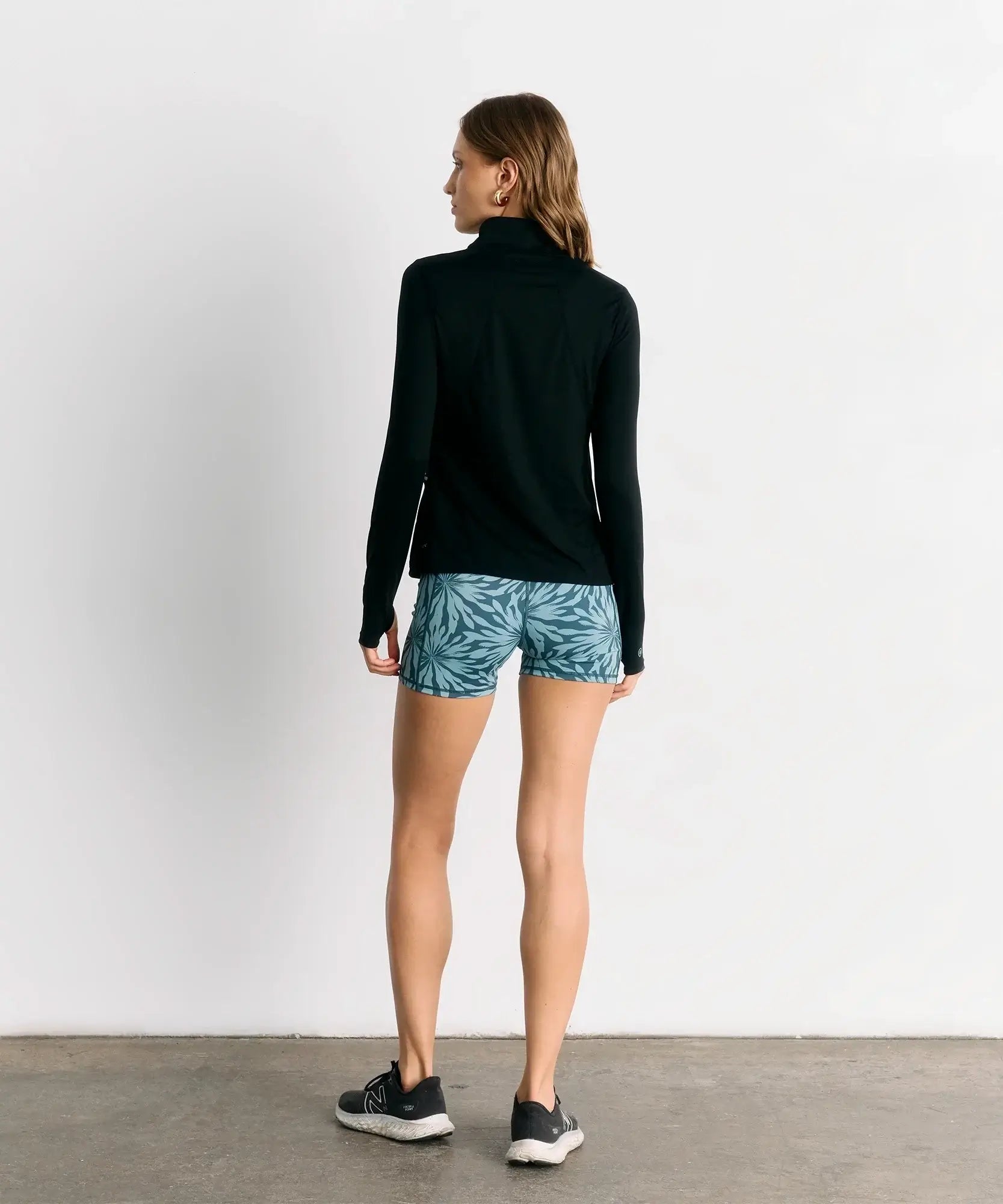 Mujer de espaldas usando el Polerón Primera Capa Active de Lounge con pantalones cortos de estampado tropical.