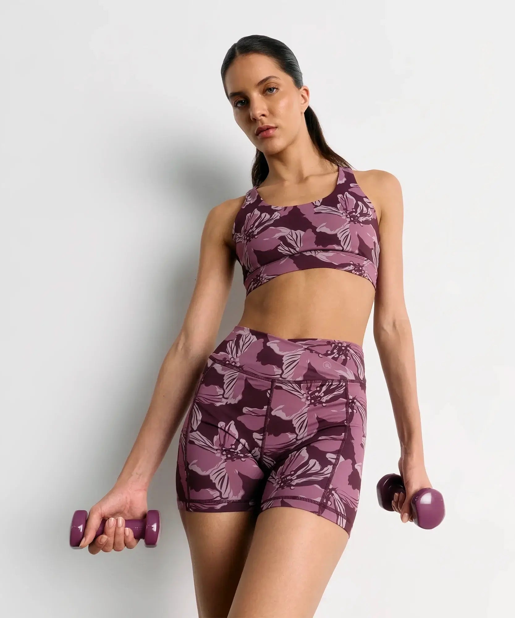 Short Deportivo Biker Flores Active de marca Lounge, modelo en color púrpura con diseño de flores, con pesas en las manos.