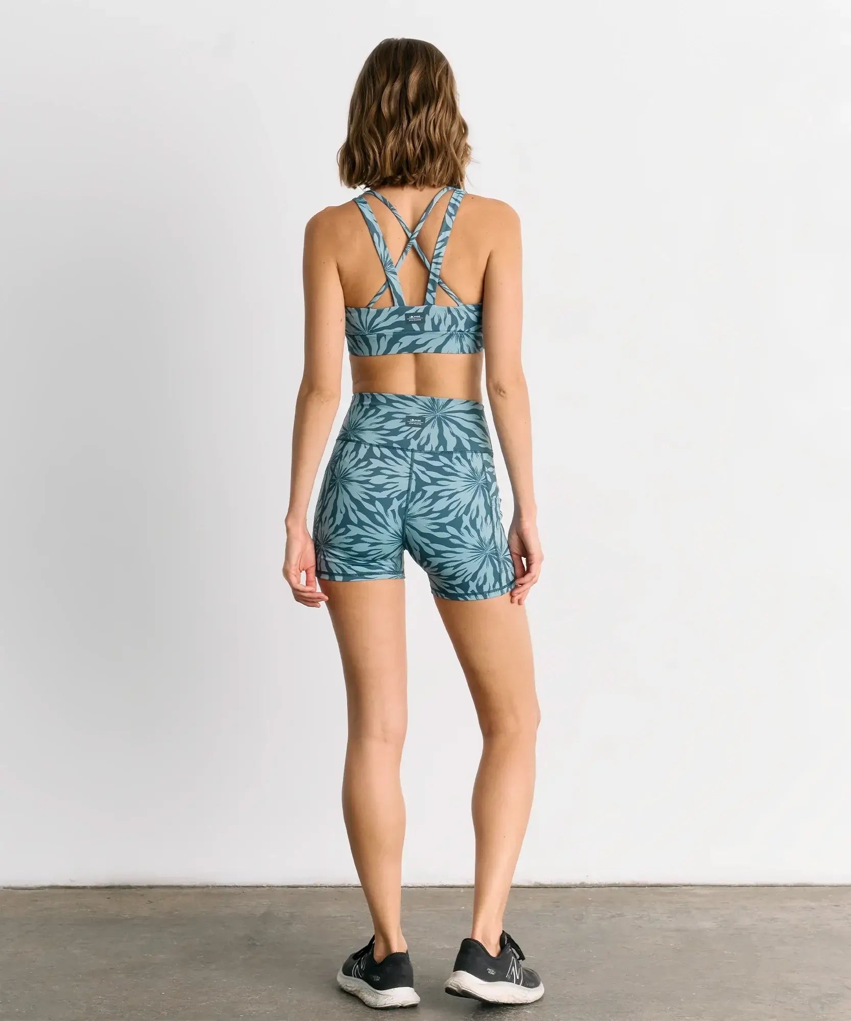 Mujer vista de espaldas usando short deportivo biker flores active de Lounge, con diseño azul y tirantes cruzados.