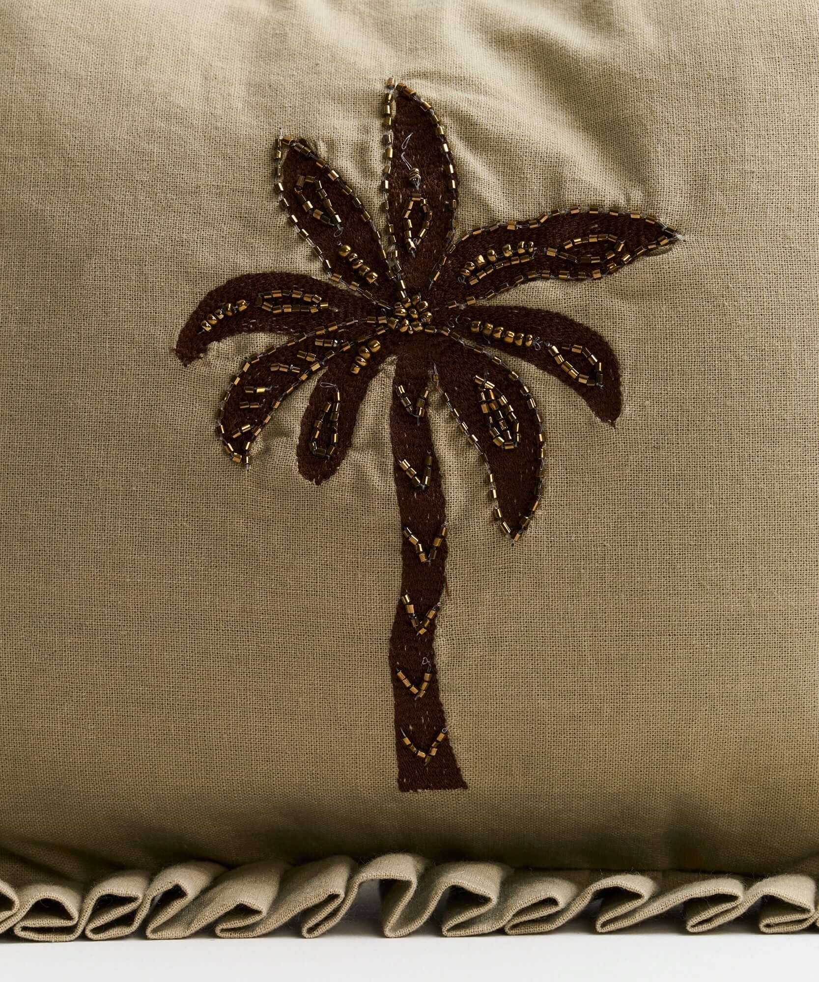 Decorative pillow with brown palm tree embroidery and ruffled edge, perfect for tropical-themed decor.