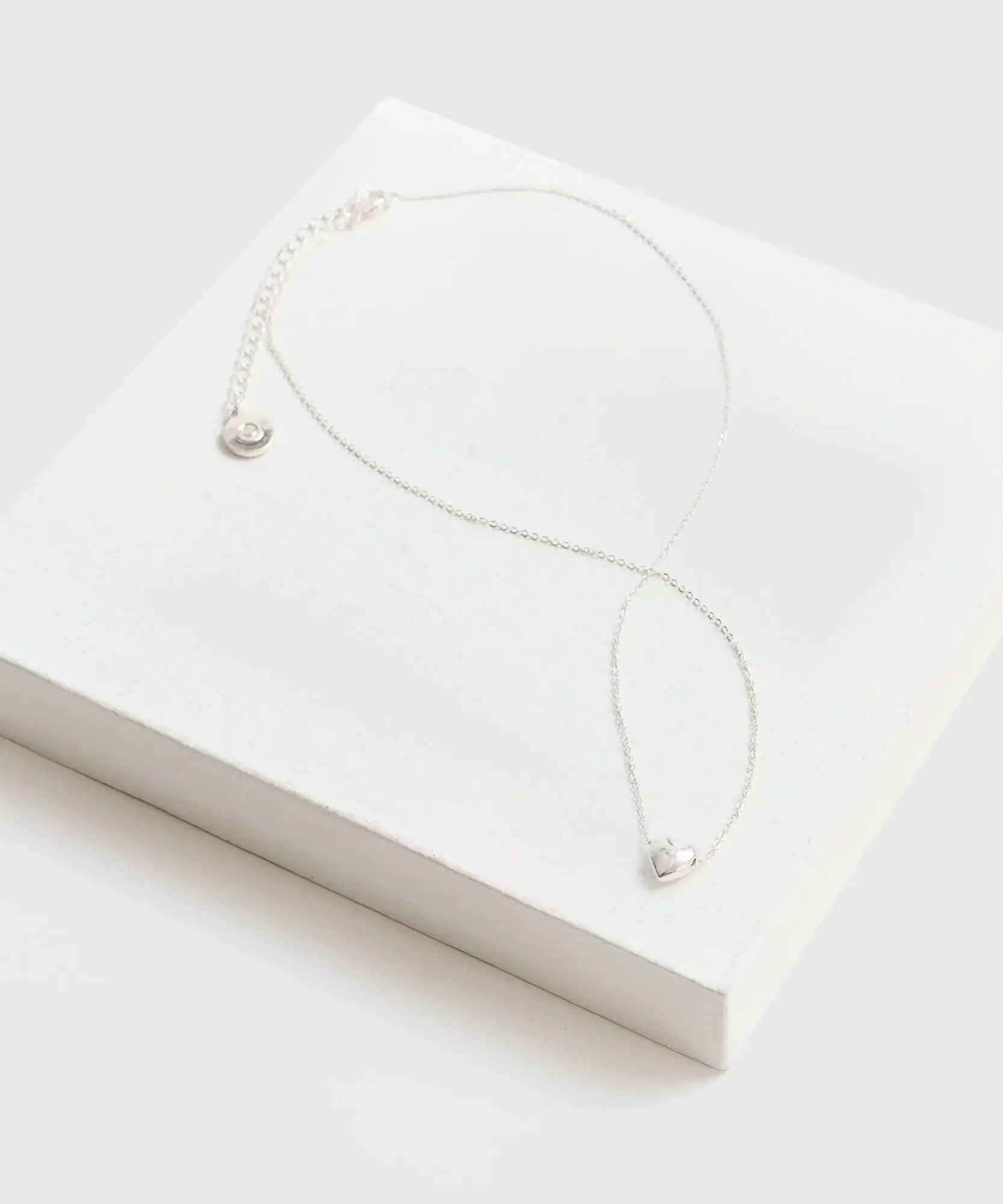 Collar Corazón de cadena delgada con charm de corazón de la marca Lounge sobre una caja blanca.