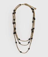 Collar Mostacillas Triple de Lounge, collar largo dorado de tres capas con mostacillas y piedras negras.
